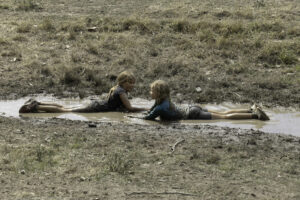 Two girls having fun, lying in a large puddle of mud